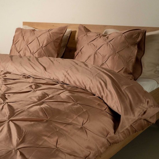 Een tweepersoonsbed met oudroze dekbedovertrek en kussenslopen met 3D-plooien, opgemaakt op een houten bedframe.