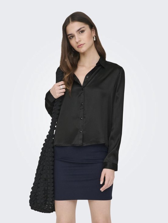 Model draagt zwarte satijnen blouse met knoopjes en donkerblauwe rok.