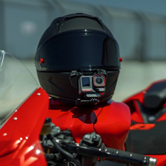 Insta360 actiecamera gemonteerd op de kin van een zwarte motorhelm op een rode motorfiets.