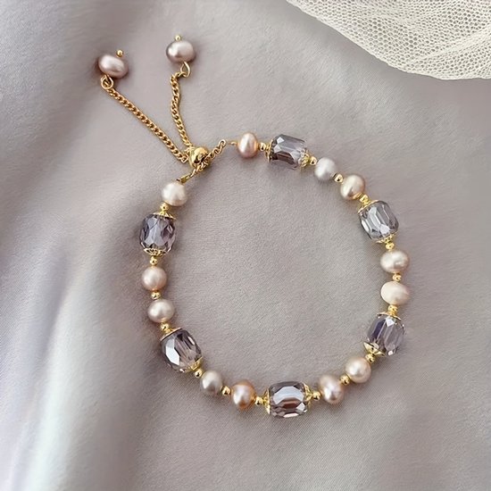 Gouden armband met parelwitte en roze parels afgewisseld met grijze facetkralen op een grijze achtergrond. Verstelbaar.