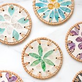 Ronde onderzetters met gevlochten rotan randen, versierd met mozaïek bloemmotieven in blauw, paars en groen.