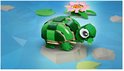 Groene LEGO-schildpad met grote ogen op een grijze steen, naast een roze waterlelie in blauw water.
