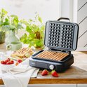 Open zwart wafelijzer met twee wafelvormige vakken opgemaakt met fruit en slagroom.