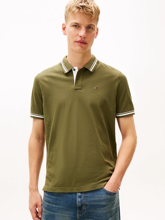Een man met kort blond haar draagt een olijfgroene polo en jeans.