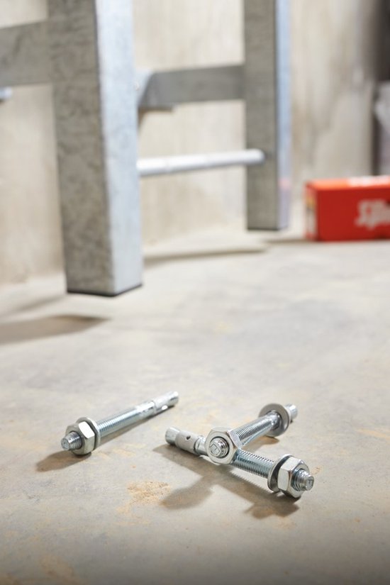 Drie metalen pluggen met moeren en ringen op een betonnen vloer, dichtbij een metalen frame.