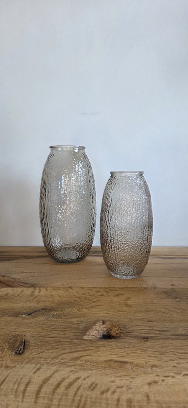Twee ovale glazen vazen met een ruw, bobbelig oppervlak, staand op een houten tafel naast een witte muur.