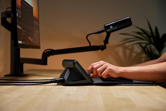 Zwarte Elgato XLR Dock MK.2 met microfoon op een arm en een persoon die een toetsenbord gebruikt.