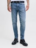 Man met tatoeages draagt een lichtblauwe skinny jeans met riem en zwarte schoenen.
