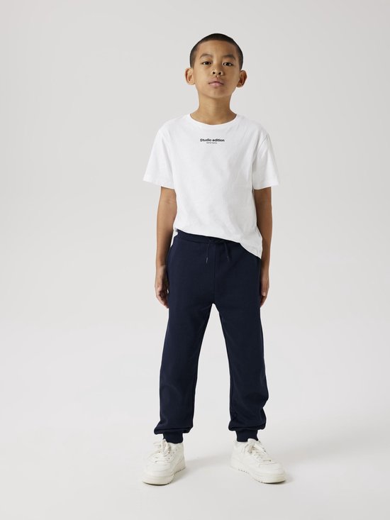 Jongen in een wit T-shirt en donkerblauwe joggingbroek met koord.
