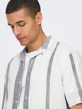 Detail van een man met een wit kort-mouw overhemd met verticale grijze strepen. Wit T-shirt eronder.