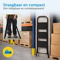 Zwarte metalen huishoudtrap met 3 treden, ingeklapt en in een magazijnomgeving.