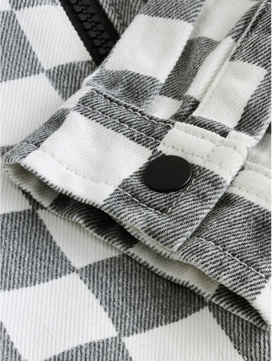 Detailopname van de mouwboord met een zwarte knoop op het grijs-witte overshirt.