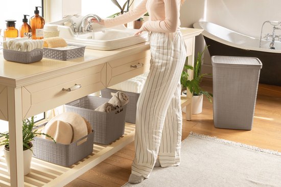 Vrouw bij een wastafel met gestreepte broek, textiele manden en een grijze wasmand.