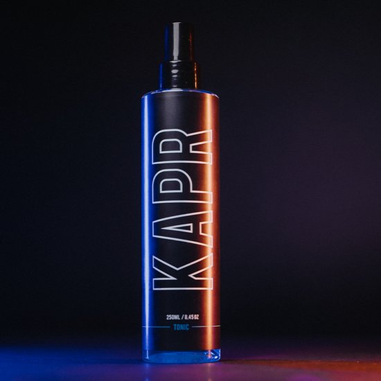 Zwarte KAPR Tonic fles met witte letters, verlicht door blauwe en oranje lampen.