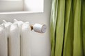 Netatmo slimme thermostaatknop, zilverkleurig met oranje accent, op een oude crèmekleurige radiator.