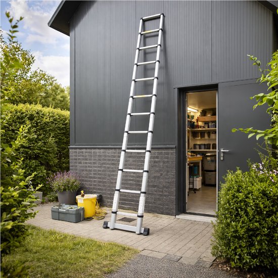 Volledig uitgeschoven Mexxo telescoopladder tegen een grijze schuur, met een openstaande deur en beplanting.