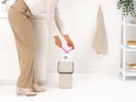 Vrouw sluit een licht beige prullenbak met een afvalzak met trekkoord.