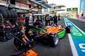 Een oranje en groene formule 1 auto wordt onderhouden door monteurs in een pitstraat.