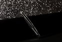 Tweezerman schuin pincet met zwarte glitter, op een donkere ondergrond met glitter bokeh effect.