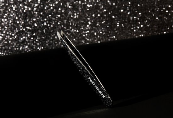 Tweezerman schuin pincet met zwarte glitter, op een donkere ondergrond met glitter bokeh effect.