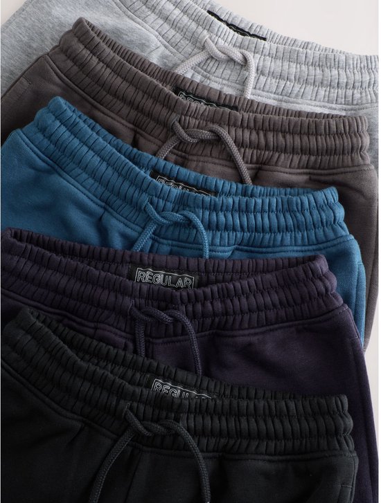 Close-up van de taillebanden met trekkoorden van vijf joggingbroeken in verschillende kleuren.