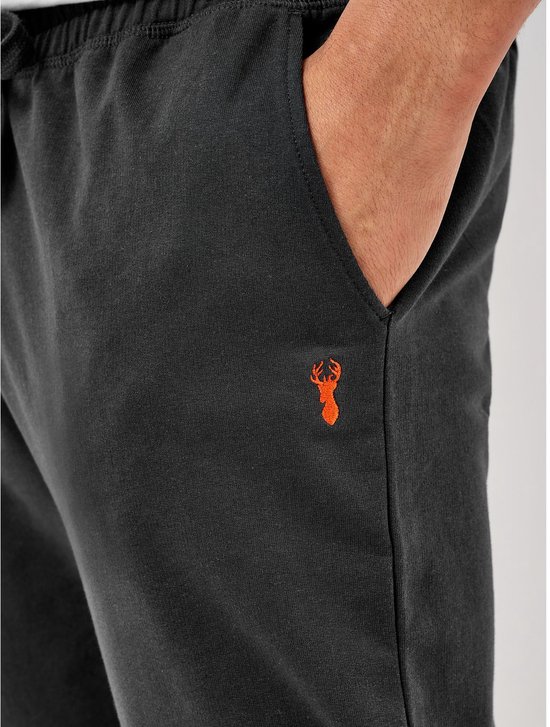 Close-up van de heup van een donkergrijze joggingbroek met een oranje rendierlogo en een hand in de zak.