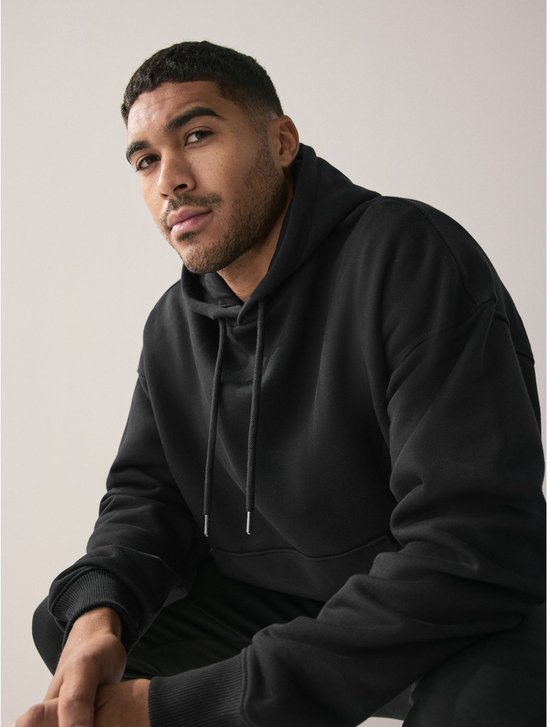 Man die op een bankje zit en een zwarte oversized hoodie met capuchon draagt.