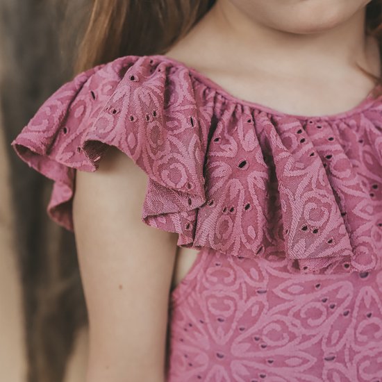 Close-up van een roze badpak met broderie en ruches op de schouder.