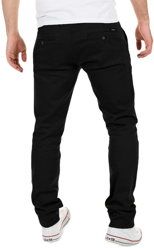 Achterkant van een man in een zwarte slim fit chinobroek en witte sneakers. De broek heeft twee achterzakken.