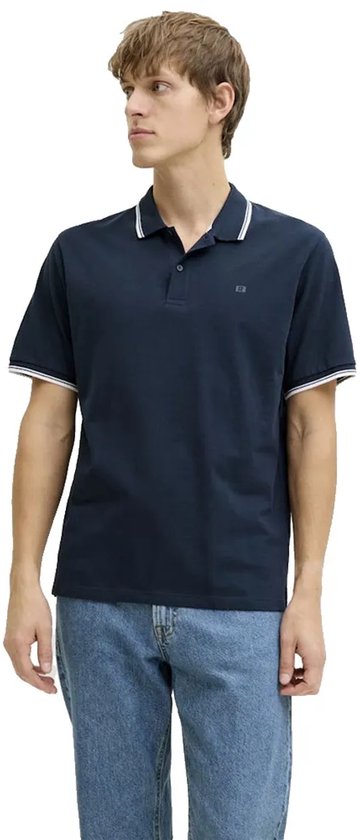 Man in donkerblauw poloshirt met witte streepdetails op kraag en mouwen, en blauwe jeans.