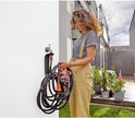 Vrouw met krullend haar, bijpassende tuinbroek en gestreepte top, houdt een donkergrijze textielslang met oranje spuitmond vast.