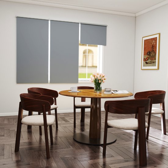 Grijze rolgordijnen boven een raam in een eetkamer met een ronde tafel en vier houten stoelen.