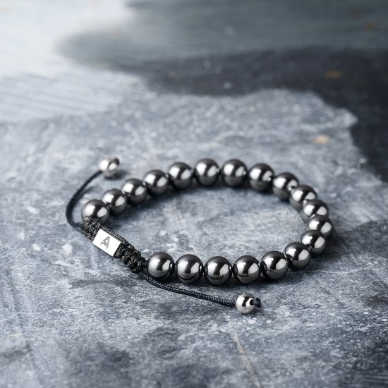 Donkere, glanzende kralenarmband met zwarte koord en een zilverkleurig vierkant bedeltje met de letter A.