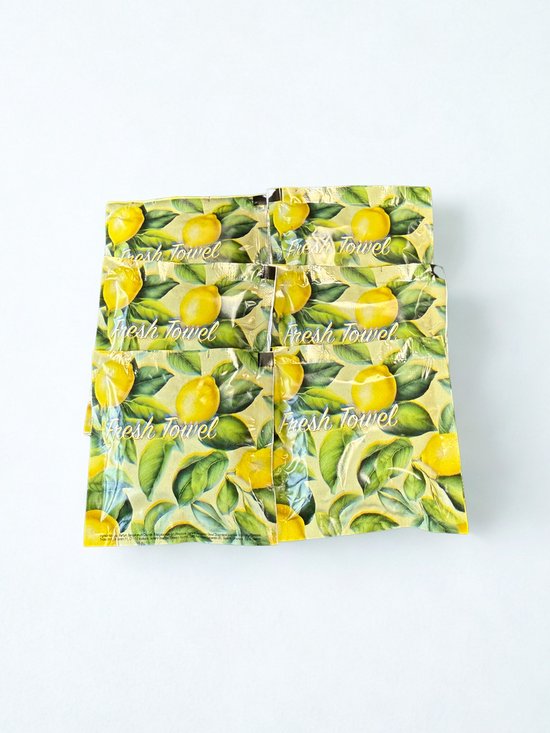 Une pile de six lingettes emballées individuellement avec un motif jaune vif de citrons et de feuilles vertes. Le texte "Fresh Towel" est visible.