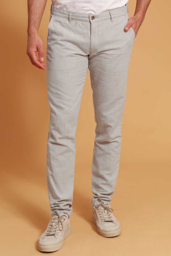 Een man in een beige linnen broek en witte sneakers, met de hand in zijn zak.