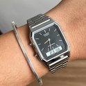 Main avec montre argentée avec bracelet métallique, cadran noir, heure analogique et numérique, à côté d'un bracelet argenté.