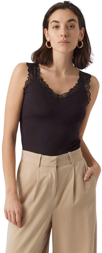 Model met donkerbruin haar en gouden oorbellen draagt een zwarte tanktop met kanten rand, met de hand in de zak van de beige broek.