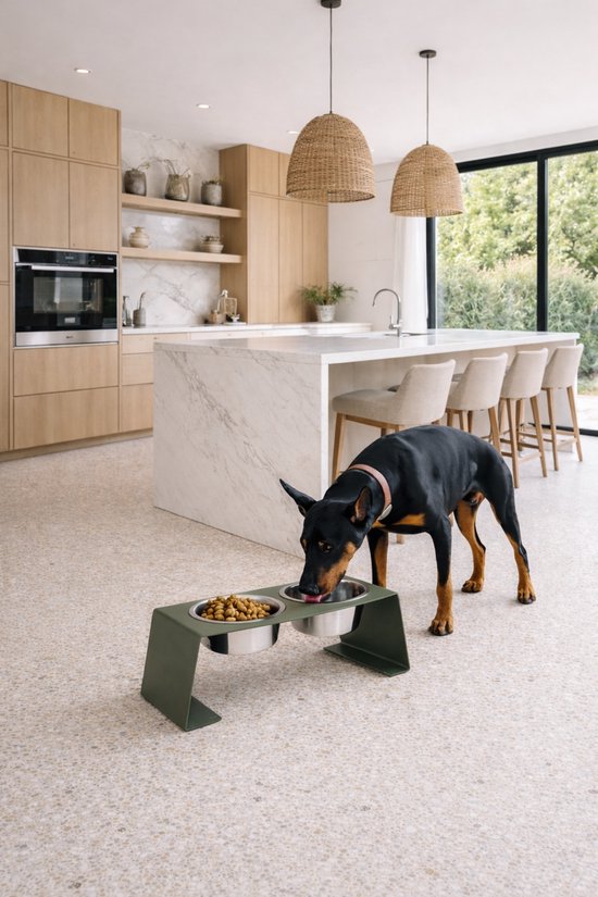 Zwarte Dobermann eet uit een dubbele voerbak op een verhoogd groen station in een moderne keuken.