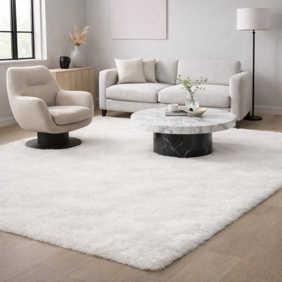 Tapis blanc duveteux à poils longs, dans un salon lumineux et moderne avec canapé et fauteuil.