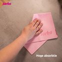 Hand die een roze Sorbo microvezeldoek gebruikt op een nat aanrecht.