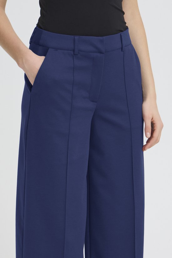 Close-up van de voorkant van een donkerblauwe, wijde broek met rechte pijpen en een hoge taille, met de handen in de zakken.