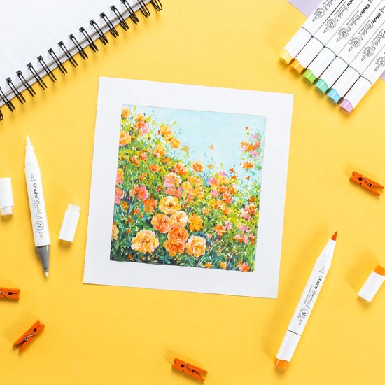Een schilderij van oranje bloemen naast markers en een notitieboek op een gele achtergrond.