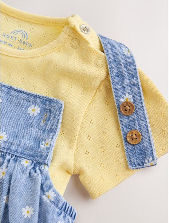Detail van de Next baby-body met tekst, drukknopen op de schouder en houten knopen op de tuinbroekband.