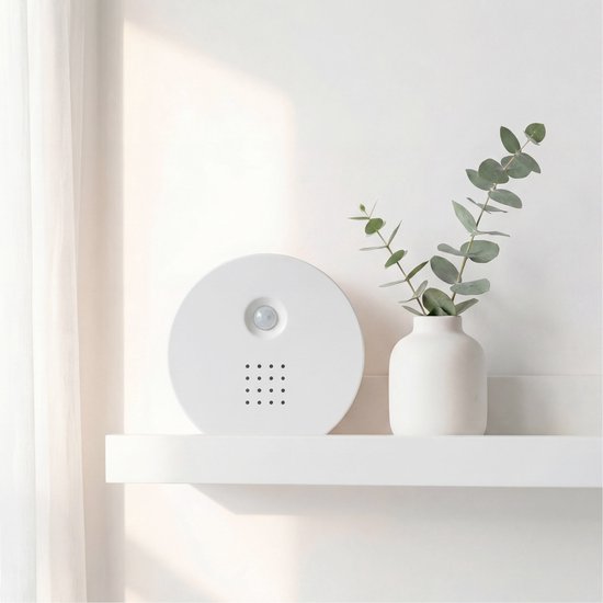 Wit, rond geluidshuisje met sensor op een witte plank, naast een vaas met eucalyptus.