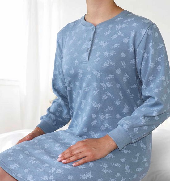 Model zittend op bed, draagt een lichtblauwe nachtjapon met bloemenprint en lange mouwen.