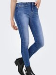 Zijaanzicht van een skinny jeans met een blauwe denim wassing en rafelige zoom, gedragen door een model met zwarte laarsjes.