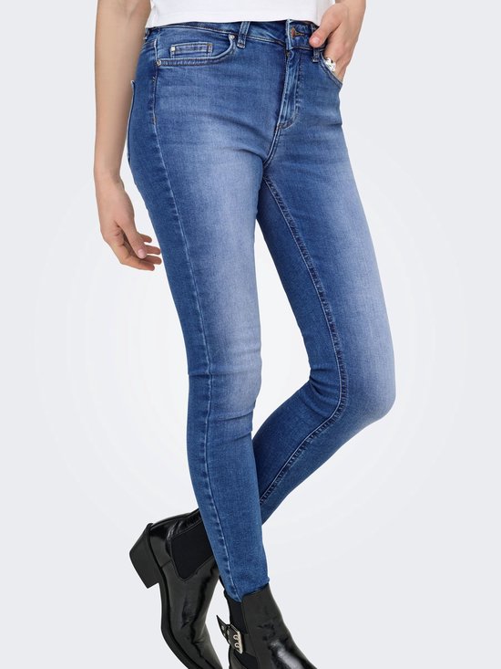 Zijaanzicht van een skinny jeans met een blauwe denim wassing en rafelige zoom, gedragen door een model met zwarte laarsjes.