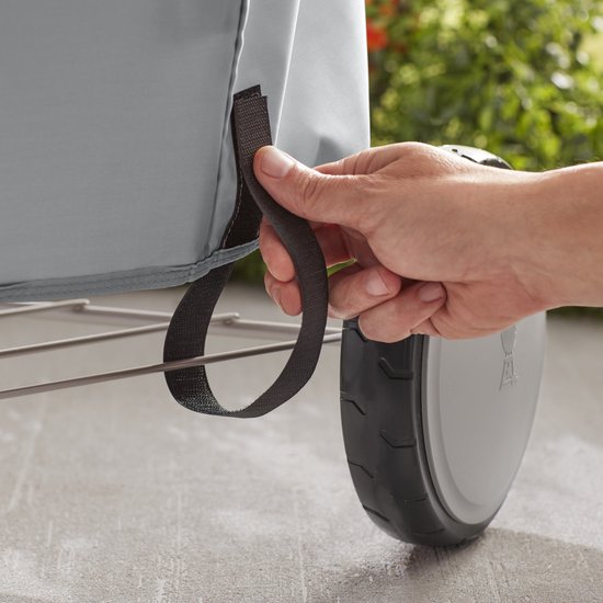 Hand trekt aan een bevestigingslus van een grijze Weber barbecuehoes.