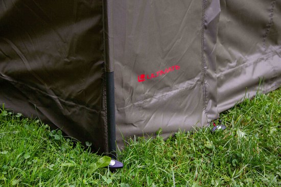 Zijkant van een groene tent met rode 'ULTIMATE' logo en grondpinnen.