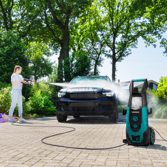 Vrouw met linnen hemd en spijkerbroek reinigt zwarte auto met groene en zwarte hogedrukreiniger.